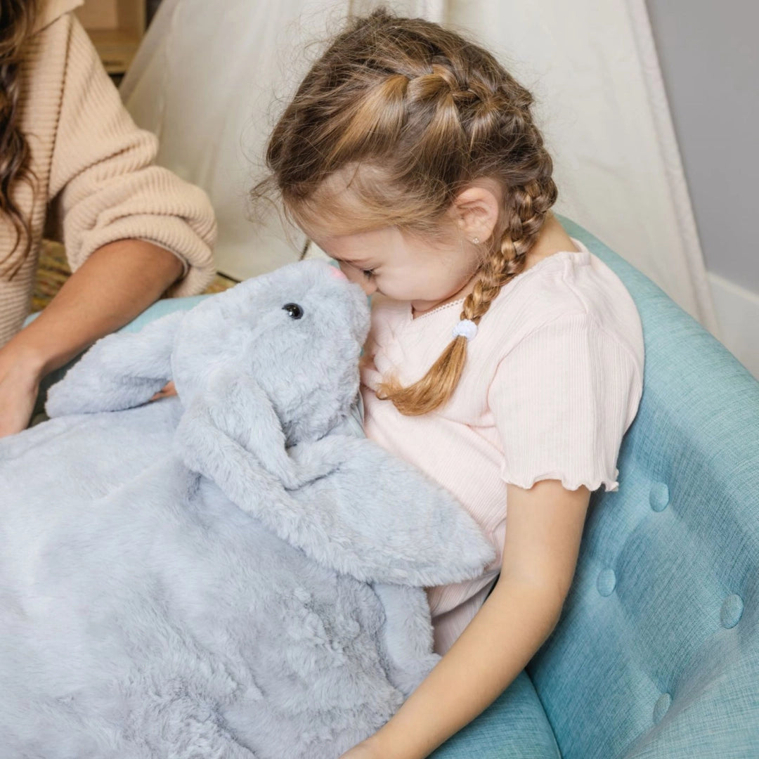 Young girl sitting on a blue chair holding a gray weighted lap bunny sensory toy