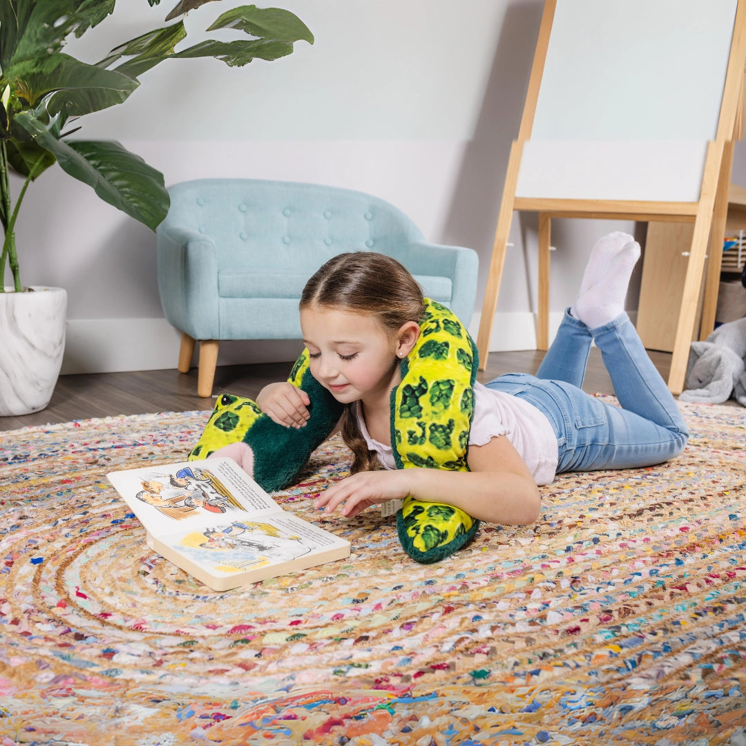 Child reading a book on the floor with a calming snake weighted plush, sensory toy for focus and relaxation.
