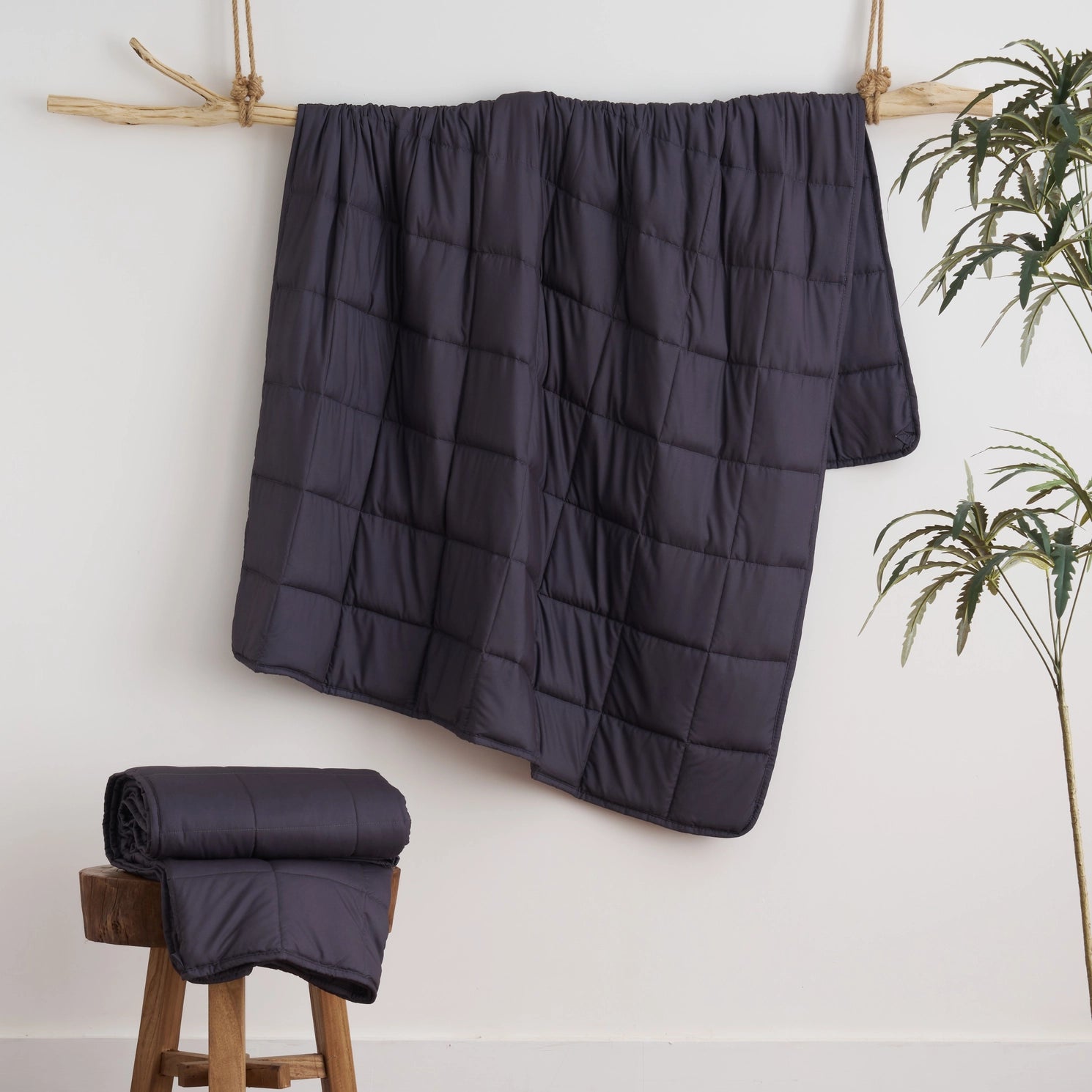 Dark charcoal gray weighted blanket draped over a wooden frame beside a plant — modern calming blanket for sleep, stress, and anxiety relief.