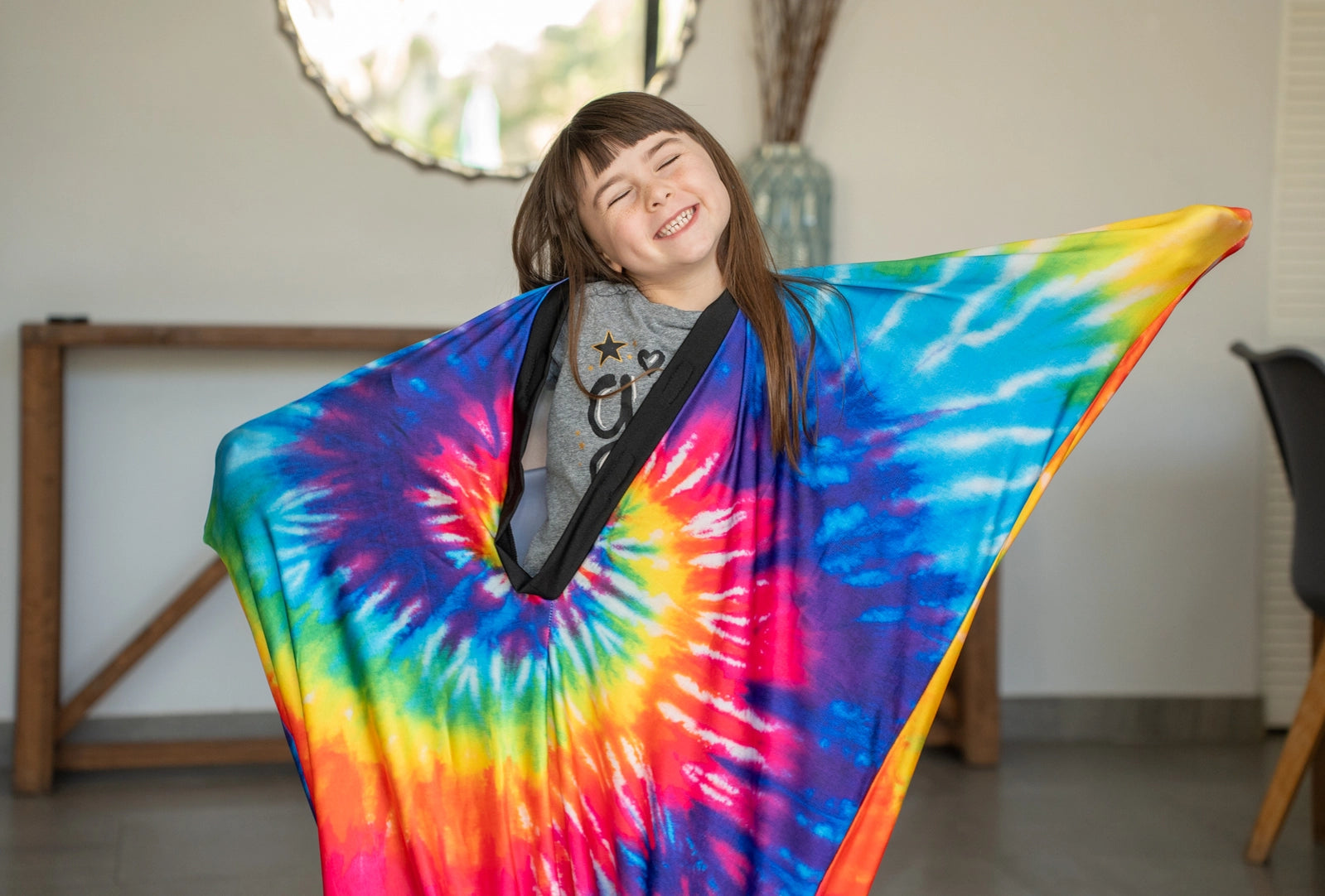 Child smiling indoors while wearing a tie-dye sensory compression blanket, promoting calm, focus, and fun play.