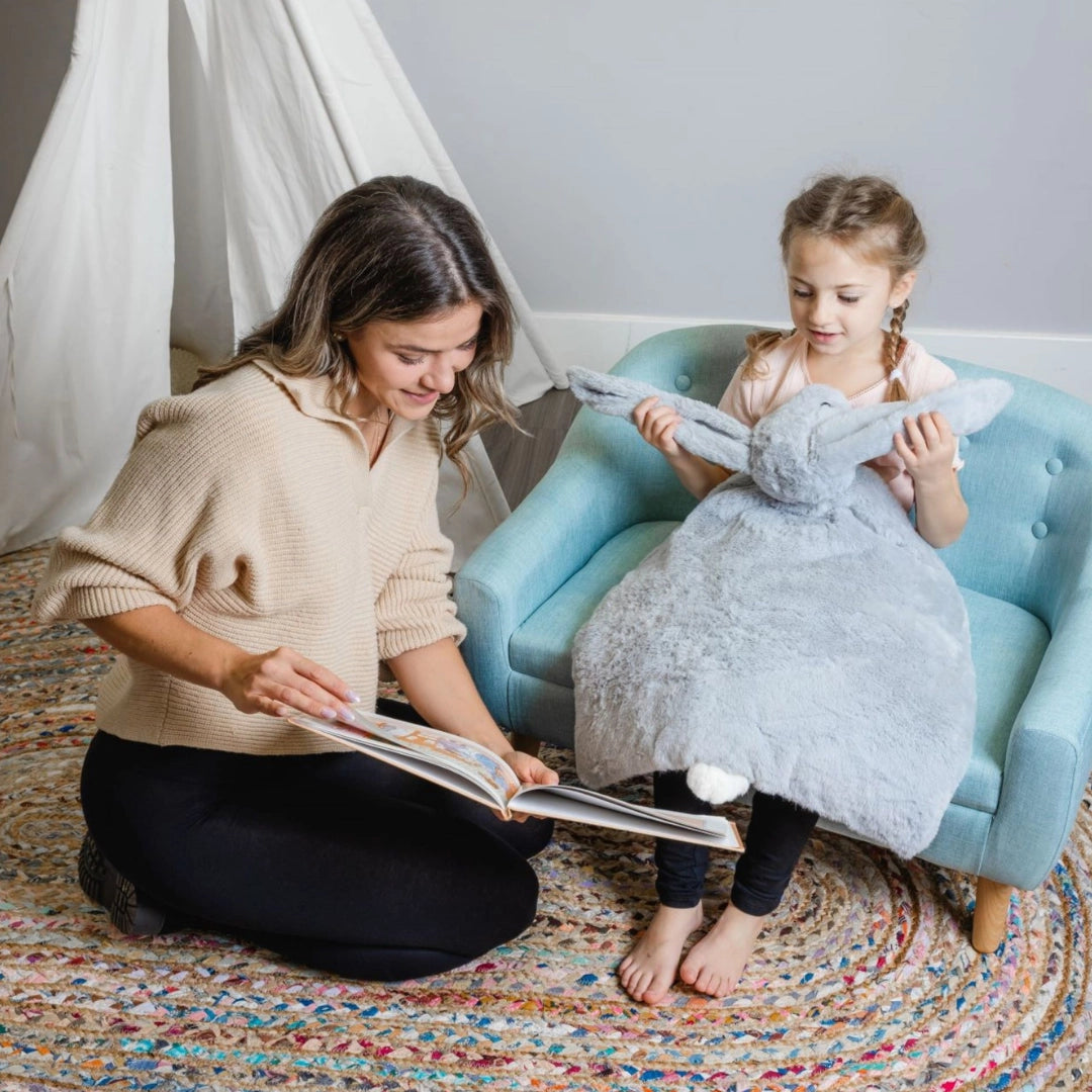 Mother reading a book with young daughter holding a weighted lap bunny sensory tool on a cozy rug